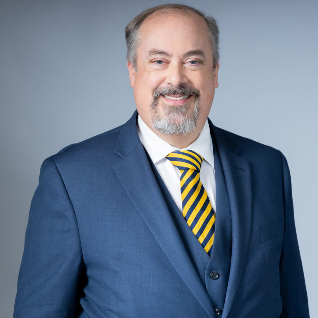 image of slightly balding man in his 50s in a blue suit, white shirt and yellow and black striped tie