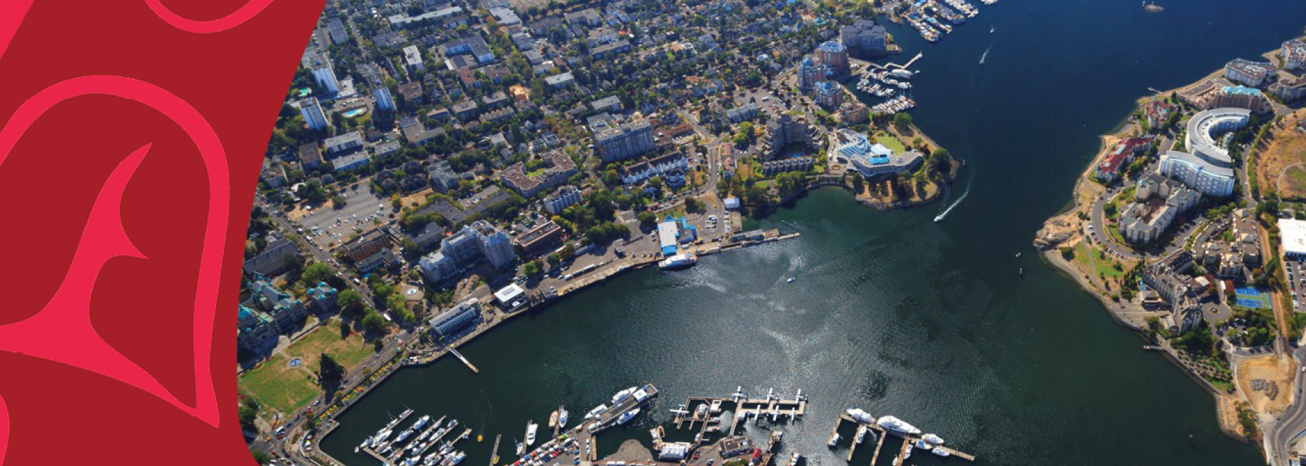 Aerial view of a coastal harbor and downtown waterfront, with marinas filled with boats, dense urban development, and roads surrounding a large inlet. A narrow waterway extends into the distance between two shorelines lined with residential and commercial buildings. The left side of the image features a decorative red and pink graphic overlay, while the harbor and cityscape dominate the remainder of the scene under clear daylight.